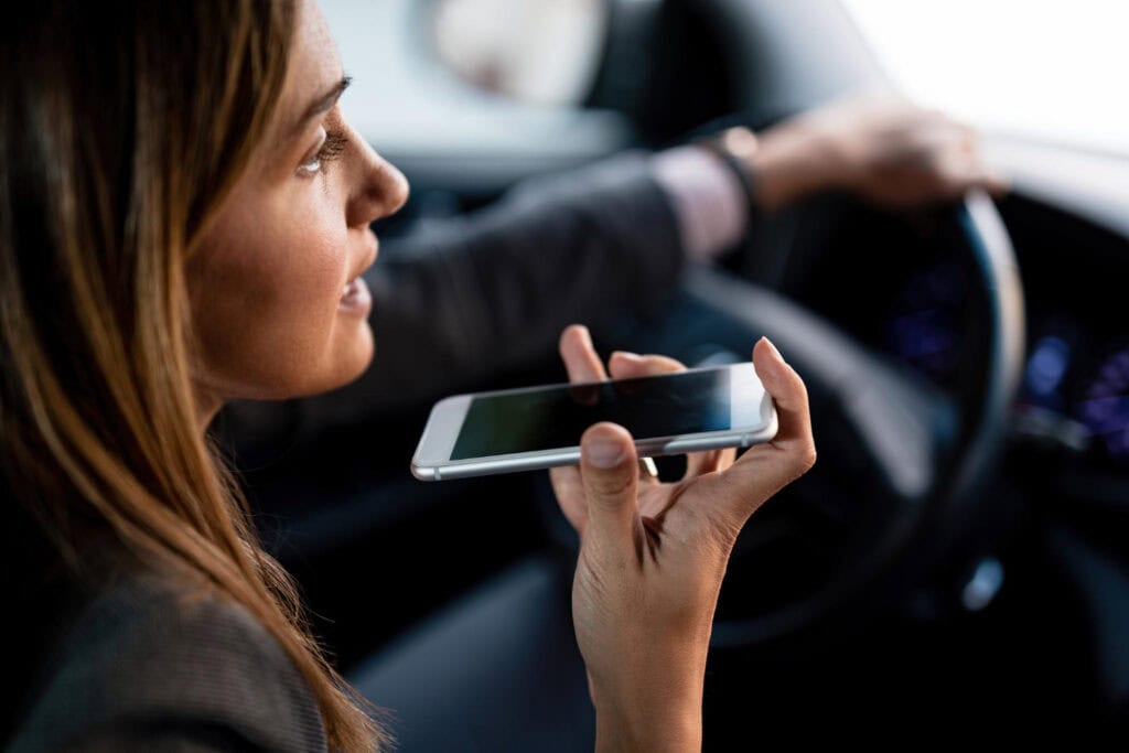 Woman using voice command on her smartphone while driving, illustrating distracted driving behavior.