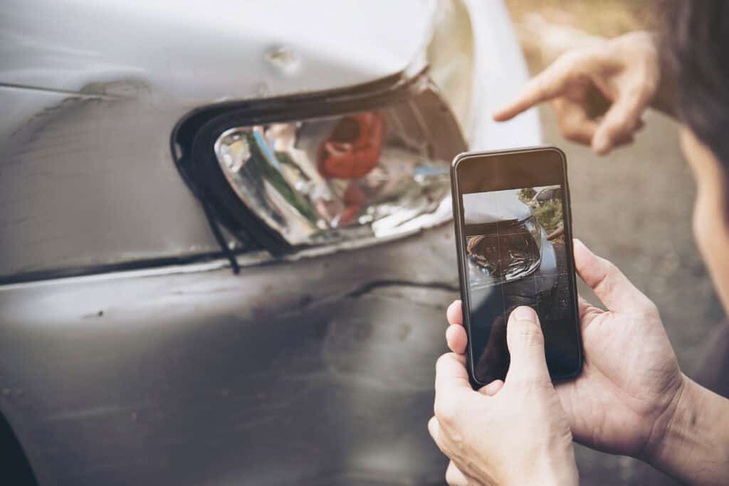 Close-up of a person taking a photo of car damage for accident documentation and insurance claim.