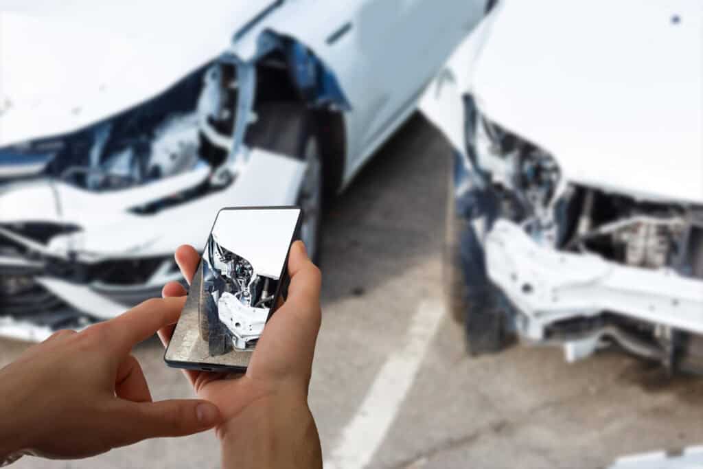 Accident victim collecting visual evidence by photographing vehicle damage after a crash.